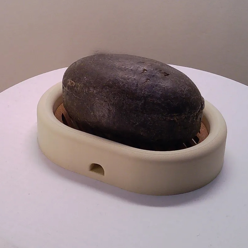 3D-printed oval soap dish with drain rack, white and wood-look.